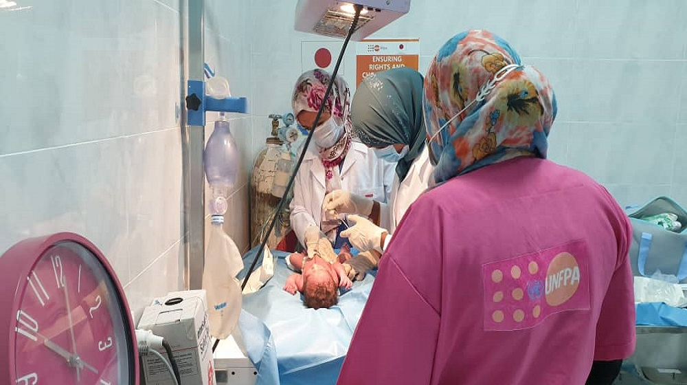 Teams of health care workers, including obstetricians/gynecologists and midwives intensely observing a newly borned baby