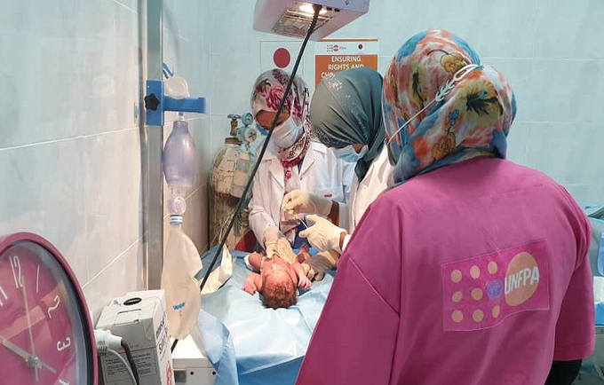 Teams of health care workers, including obstetricians/gynecologists and midwives intensely observing a newly borned baby